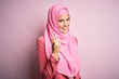 © Krakenimages.com - Young beautiful girl wearing muslim hijab standing over isolated pink background Beckoning come here gesture with hand inviting welcoming happy and smiling