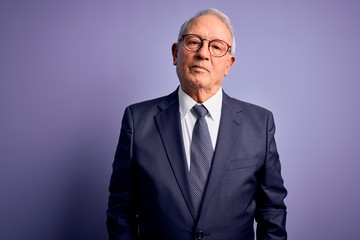 Canvas Print - Grey haired senior business man wearing glasses and elegant suit and tie over purple background Relaxed with serious expression on face. Simple and natural looking at the camera.