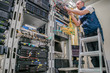 Technician standing on a ladder connects internet wires. The specialist works in the server room of the data center. Worker lays communication cables. Technological concept.