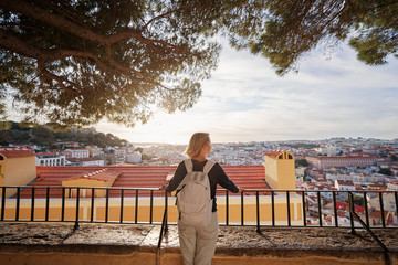 Wall Mural - Traveling by Portugal. Young traveling woman enjoying old town Lisbon view, red tiled roofs and ancient architecture.