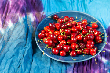 Canvas Print - Blue plate with red ripe cherries on textile background