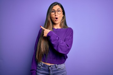 Wall Mural - Young beautiful smart woman wearing glasses over purple isolated background Surprised pointing with finger to the side, open mouth amazed expression.