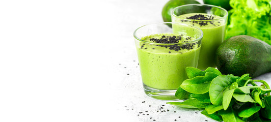 Green smoothie of avocado, spinach and seeds in glasses and spinach leaves on a gray concrete table. Healthy eating, raw food diet and vegan food. Green vegetables smoothie. Free space for text