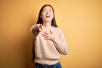 Wall Mural - Young beautiful asian woman wearing casual sweater over yellow isolated background laughing at you, pointing finger to the camera with hand over body, shame expression