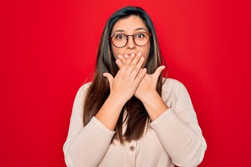 Sticker - Young hispanic smart woman wearing glasses standing over red isolated background shocked covering mouth with hands for mistake. Secret concept.