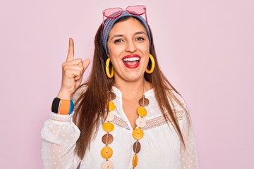 Canvas Print - Young hispanic hippie woman wearing fashion boho style and sunglasses over pink background pointing finger up with successful idea. Exited and happy. Number one.