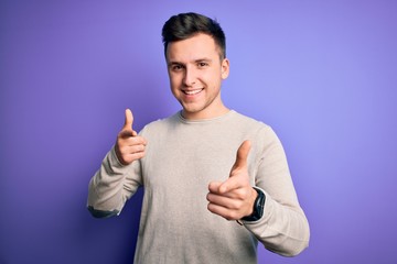 Wall Mural - Young handsome caucasian man wearing casual sweater over purple isolated background pointing fingers to camera with happy and funny face. Good energy and vibes.