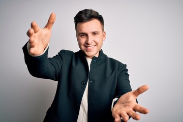 Wall Mural - Young handsome business mas wearing elegant winter coat standing over isolated background looking at the camera smiling with open arms for hug. Cheerful expression embracing happiness.