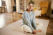 © shurkin_son - Attractive gray haired retired woman sitting barefooted on carpet at home, keeping legs crossed, stretching thighs, doing butterfly yoga exercise. Rest, relaxation, yoga, age and retirement concept
