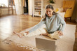© shurkin_son - Online training, technology, health and activity. Happy active barefoot mature woman sitting on floor in front of open laptop, doing yoga, repeating exercises after professional instructor on video
