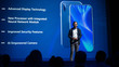 © Gorodenkoff - Live Event with New Products Reveal: Keynote Speaker Presents Smartphone Device to Audience. Movie Theater Screen Shows Mock-up Touch Screen Mobile Phone with High End Features and Top Highlights