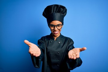 Wall Mural - Young african american chef woman wearing cooker uniform and hat over blue background smiling cheerful offering hands giving assistance and acceptance.