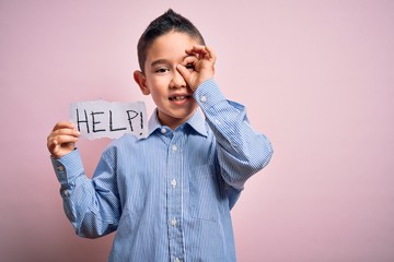 Wall Mural - Young little boy kid holding paper sing with help message asking for protection with happy face smiling doing ok sign with hand on eye looking through fingers