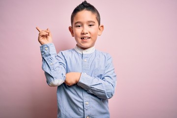 Wall Mural - Young little boy kid wearing elegant shirt standing over pink isolated background with a big smile on face, pointing with hand and finger to the side looking at the camera.