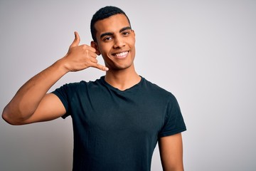 Young handsome african american man wearing casual t-shirt standing over white background smiling doing phone gesture with hand and fingers like talking on the telephone. Communicating concepts.