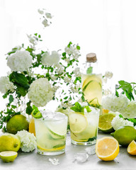 Summer composition. The table is strewn with garden flowers. Hydrangeas, jasmine, daisies in the morning sun. Fresh citrus lemonade is poured into glasses. Ice is scattered on the table. it melts, cre