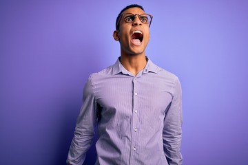 Handsome african american man wearing striped shirt and glasses over purple background angry and mad screaming frustrated and furious, shouting with anger. Rage and aggressive concept.