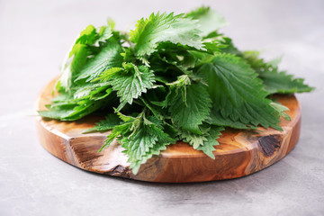 Wall Mural - Green nettle leaves in wooden pot on grey background. Alternative herbal medicine. Stinging nettles, urtica. Skin allergy care