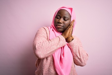 Sticker - Young african american plus size woman wearing muslim hijab over isolated pink background sleeping tired dreaming and posing with hands together while smiling with closed eyes.