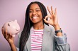 © Krakenimages.com - Young african american business woman saving money on piggy bank over isolated background doing ok sign with fingers, excellent symbol