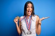 © Krakenimages.com - Young beautiful brunette atthete champion woman winning medals over blue background very happy and excited, winner expression celebrating victory screaming with big smile and raised hands