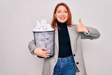 Wall Mural - Young beautiful redhead businesswoman holding full paper bin with crumpled papers happy with big smile doing ok sign, thumb up with fingers, excellent sign