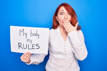 Sticker - Young redhead woman asking for women rights holding paper with my body my rules message covering mouth with hand, shocked and afraid for mistake. Surprised expression