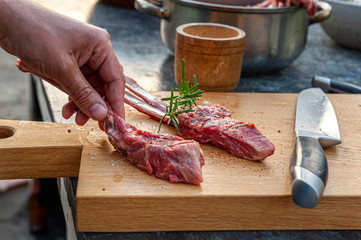 Man's hand holding lamb chops with rosemary and spices and big knife on wooden cutting board