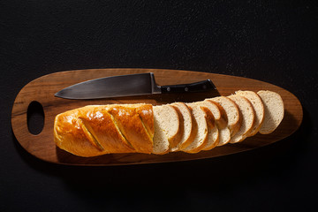 Wall Mural - sliced loaf of bread on a chopping board and a chef's knife on a black background