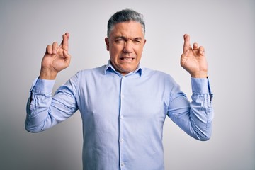 Poster - Middle age handsome grey-haired business man wearing elegant shirt over white background gesturing finger crossed smiling with hope and eyes closed. Luck and superstitious concept.