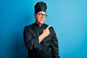 Poster - Middle age handsome grey-haired chef man wearing cooker uniform and hat Pointing with hand finger to the side showing advertisement, serious and calm face