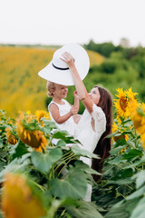 Wall Mural - Happy mother with the daughter in the field with sunflowers. mom and baby girl having fun outdoors. family concept.