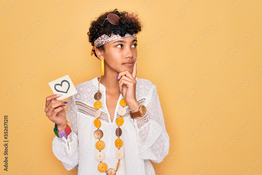 Beautiful african american afro hippie woman wearing sunglasses holding reminder with heart serious face thinking about question, very confused idea - obrazy, fototapety, plakaty 
