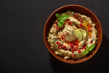 Wall Mural - homemade spread of baked eggplant baba ganoush in a bowl with pomegranate seeds, lime, olive oil and lime slices on a black background