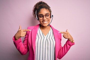 Canvas Print - Young african american call center agent girl wearing glasses working using headset looking confident with smile on face, pointing oneself with fingers proud and happy.