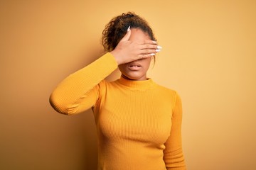 Sticker - Young beautiful african american girl wearing sweater and glasses over yellow background covering eyes with hand, looking serious and sad. Sightless, hiding and rejection concept