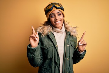 Wall Mural - Young african american afro skier girl wearing snow sportswear and ski goggles smiling confident pointing with fingers to different directions. Copy space for advertisement