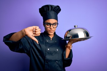 Sticker - Young african american cooker girl wearing uniform and hat holding tray with dome with angry face, negative sign showing dislike with thumbs down, rejection concept