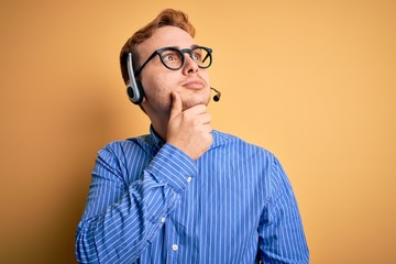 Wall Mural - Young handsome redhead call center agent man wearing glasses working using headset with hand on chin thinking about question, pensive expression. Smiling with thoughtful face. Doubt concept.