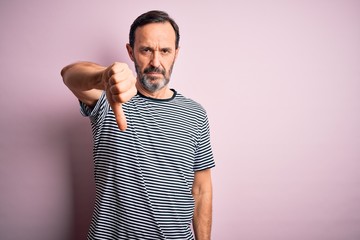 Middle age hoary man wearing casual striped t-shirt standing over isolated pink background looking unhappy and angry showing rejection and negative with thumbs down gesture. Bad expression.