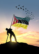 Mozambique flag turn to birds while being planted by a man on a hill during sunrise.
