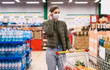 © ANR Production - Social distancing in a supermarket. A young woman in a disposable face masks and gloves with grocery basket. Shopping during the Coronavirus Covid-19 epidemic 2020