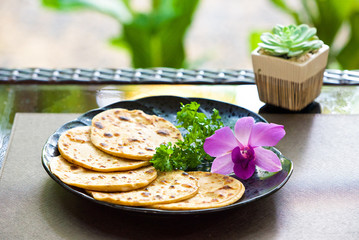 wheat flour tortillas on a black plate, chapati with dill and an orchid flower, Indian traditional bread, a plate with food on a background of flowers