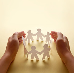 Paper people surrounded by hands in gesture of protection. Concept of insurance, social protection and support.