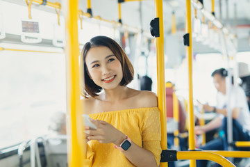 Wall Mural - Smiling beautiful woman using phone when standing on the bus.