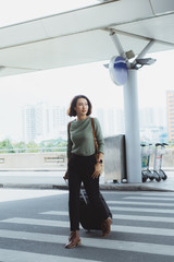 Wall Mural - Beautiful woman happily walking along pedestrian strip with suitcase and airport on background