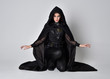 Fantasy portrait of a woman with red hair wearing dark leather assassin costume with long black cloak.  full length kneeling pose, isolated against a studio background.