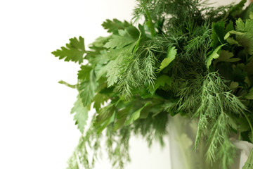 A bunch of fresh dill and parsley on the glass cup with water on the white background. Seasoning greens on the table. Healthy vegetarian food.