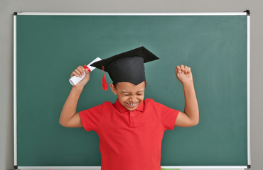 Canvas Print - Happy African-American boy in graduation hat and with diploma near chalkboard