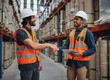 © StratfordProductions - Two cheerful man making a firm handshake in logistics workhouse holding a digital tablet in safety helmet and vest